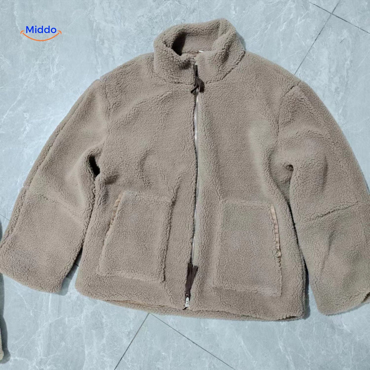 manteau teddy beige posé à plat sur le sol, aperçu du tombé et de la matière