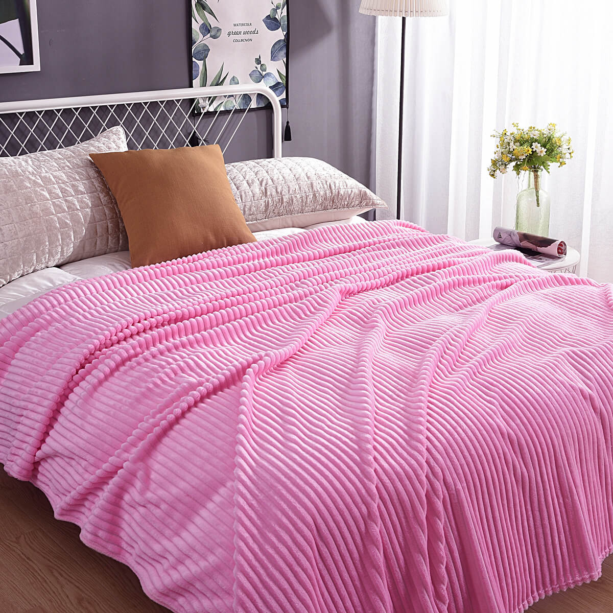 plaid en velours polaire rose tendre sur un lit avec coussins et décorations végétales