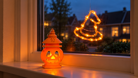 Lanterne PumpkinGlow sur un rebord de fenêtre avec un chapeau PumpkoGlow lumineux sur la vitre
