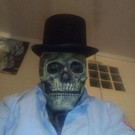 Personne portant un masque tête de mort réaliste et un chapeau haut-de-forme noir comme costume effrayant d’Halloween