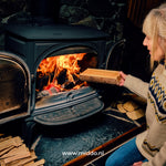 Vrouw gooit een gekloofd stuk hout in de kachel