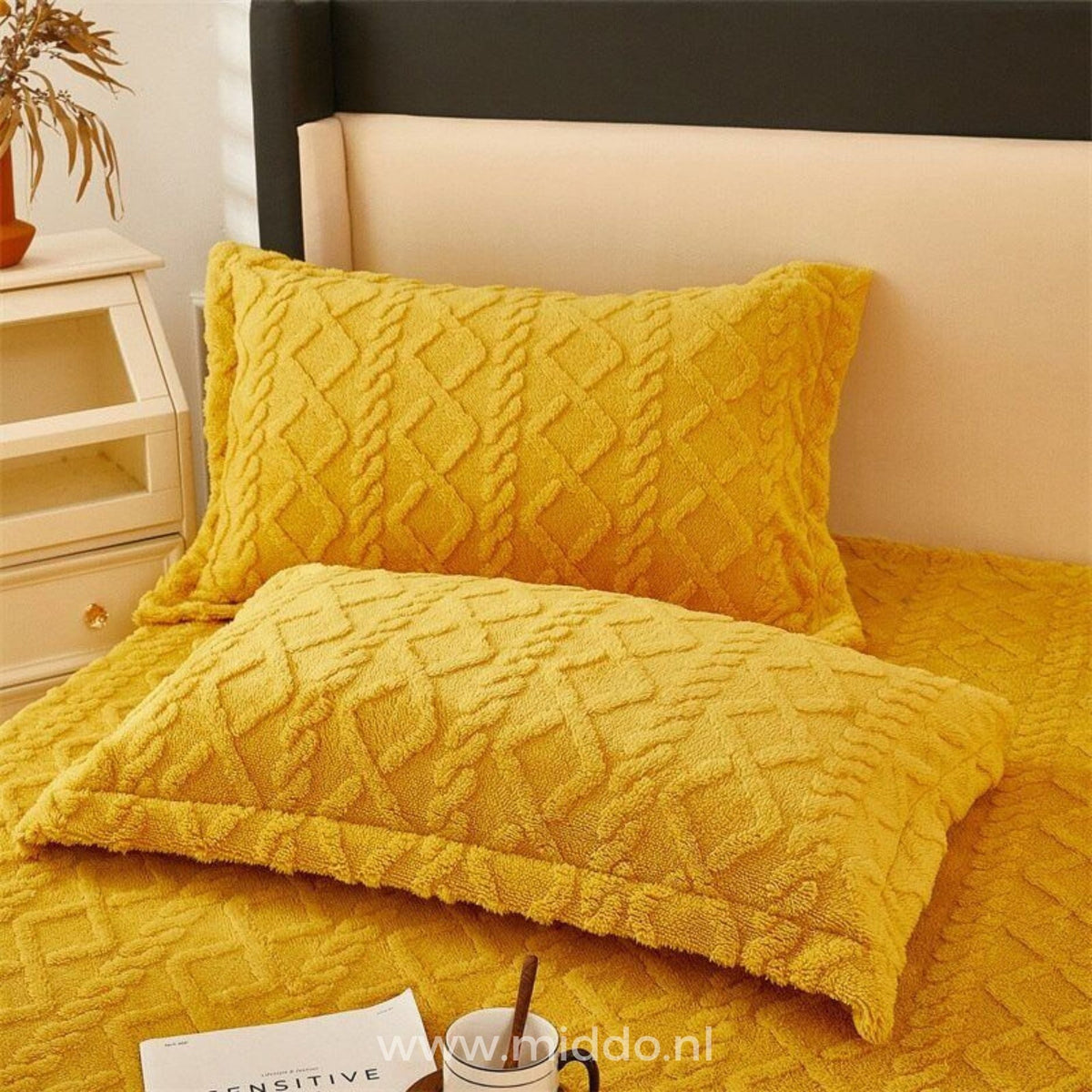 Deux taies d'oreiller jaune ocre à motif torsadé sur un lit avec drap-housse assorti