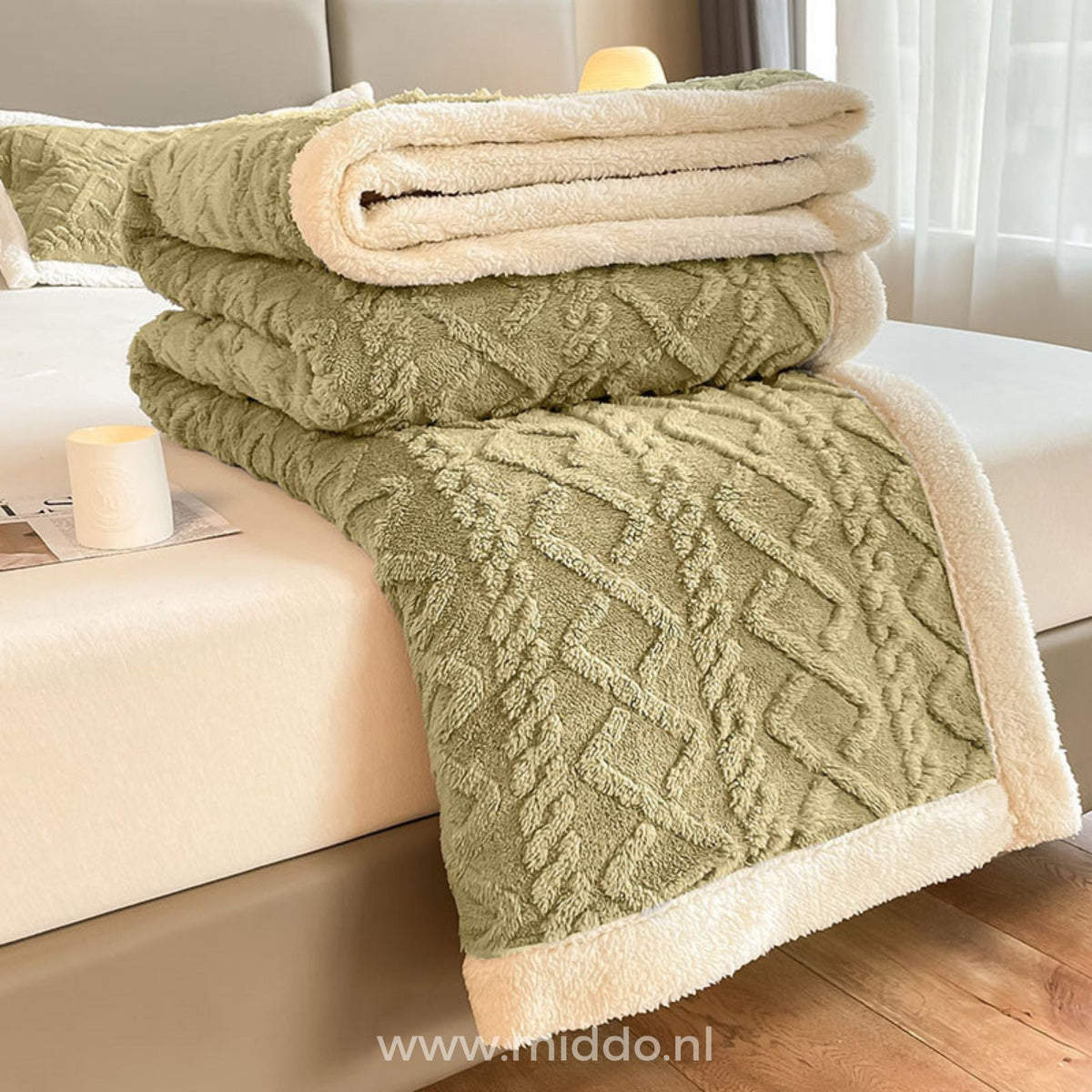 Drap-housse en polaire vert sauge plié avec doublure sherpa crème sur un lit, accompagné d'une bougie