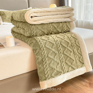 Drap-housse en polaire vert sauge plié avec doublure sherpa crème sur un lit, accompagné d'une bougie