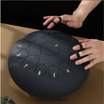 Handen bespelen een zwarte Harmonii KlankOase Steel Tongue Drum met finger picks