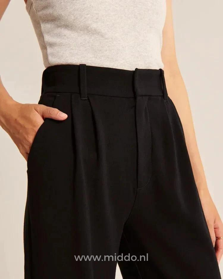 foto van vrouw in zwarte wijde pantalon gezien vanaf de middel en heeft haar hand in de steekzak.