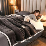 couverture en laine peluche gris foncé sur un lit avec personne endormie