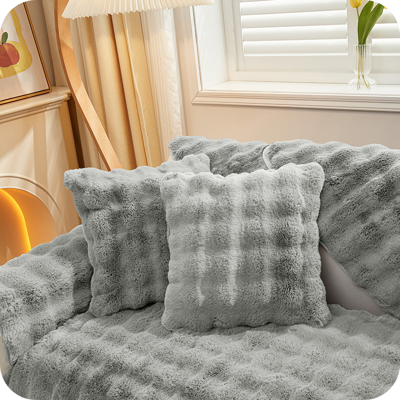 coussins et plaid gris moelleux sur un canapé près d'une fenêtre pour une ambiance hivernale