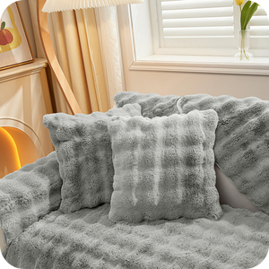coussins et plaid gris moelleux sur un canapé près d'une fenêtre pour une ambiance hivernale