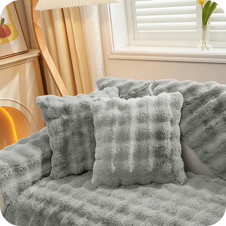 coussins et plaid gris moelleux sur un canapé près d'une fenêtre pour une ambiance hivernale
