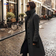 manteau gris long porté par une femme marchant dans une rue de ville