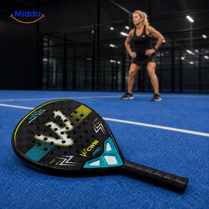 ApexTour raquette de padel: raquette sur le terrain avec une joueuse à l’arrière-plan.