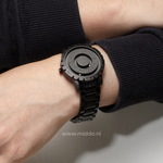 montre magnétique noire portée au poignet, bracelet métal et cadran sans chiffres