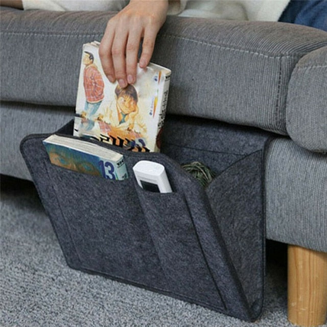 organisateur gris avec deux livres et une télécommande suspendu au côté d'un canapé gris