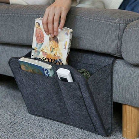 organisateur gris avec deux livres et une télécommande suspendu au côté d'un canapé gris