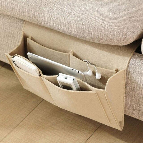 organisateur de lit beige suspendu au bord d'un canapé avec une tablette et un téléphone à l'intérieur