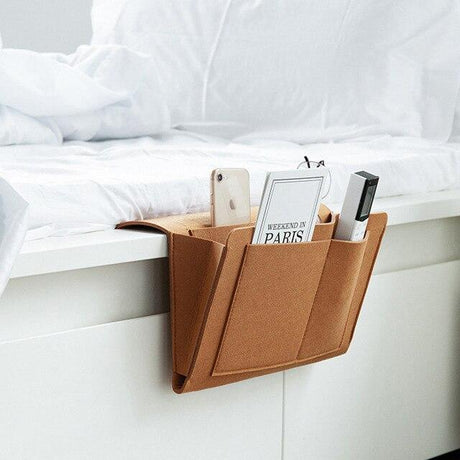 organisateur marron en cuir suspendu au bord d'un lit blanc avec accessoires à l'intérieur