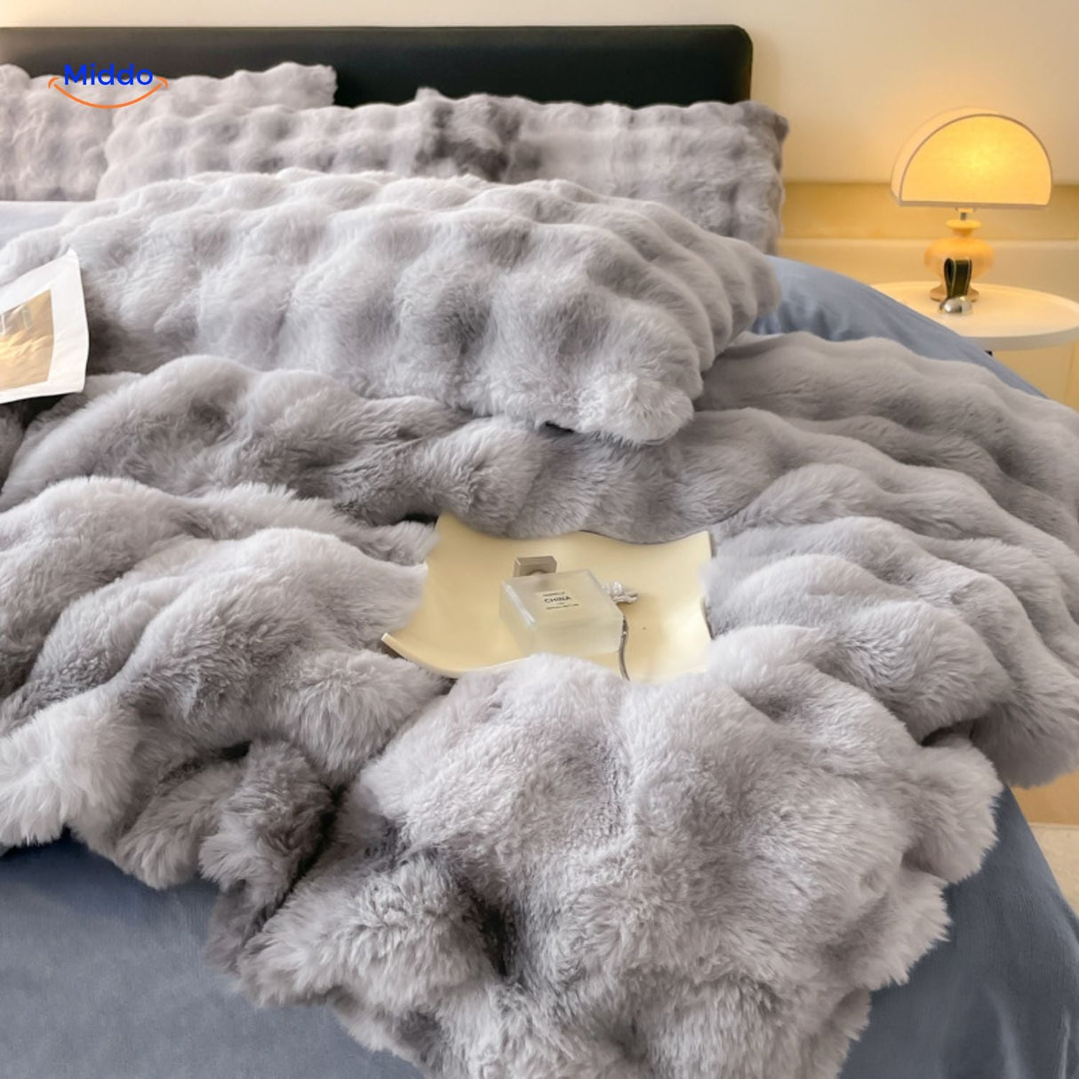 couverture en peluche grise mise en scène avec une lampe de chevet créant une ambiance cosy