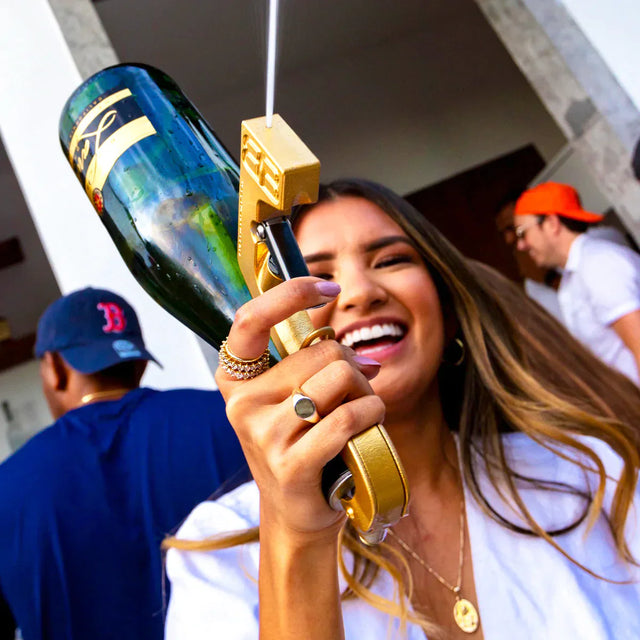 femme souriante en fête tenant un pistolet à boissons doré avec une bouteille de champagne