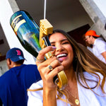 femme souriante en fête tenant un pistolet à boissons doré avec une bouteille de champagne