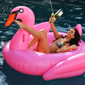 femme sur un cygne gonflable rose tenant un pistolet à boissons doré au bord de la piscine