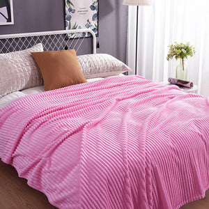 plaid en velours polaire rose tendre sur un lit avec coussins et décorations végétales