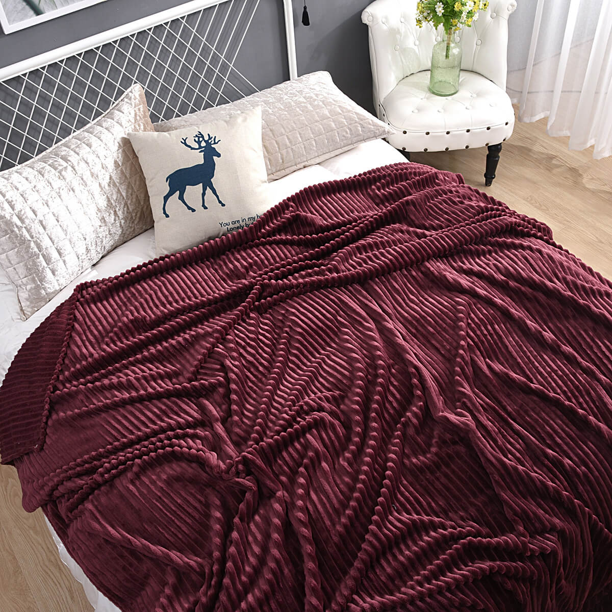 plaid en velours polaire rouge foncé sur un lit décoré de coussins motif renne, style chaleureux