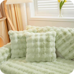 Groene pluche kussens en deken op een bank bij een raam