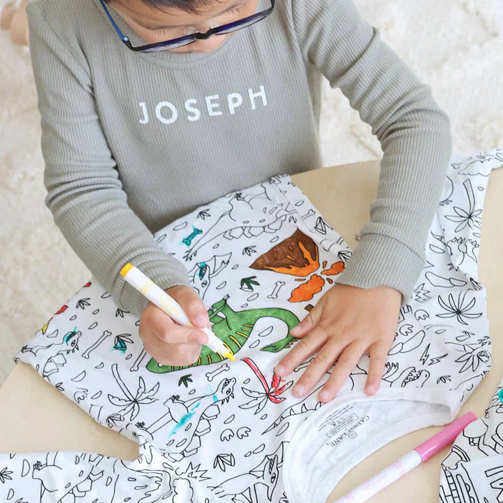 garçon en train de colorier son pyjama à colorier motif dinosaures avec des feutres textiles