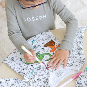garçon en train de colorier son pyjama à colorier motif dinosaures avec des feutres textiles