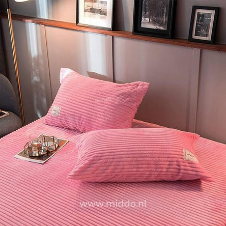 deux oreillers habillés de taies d'oreiller en velours polaire rose, posés sur un lit