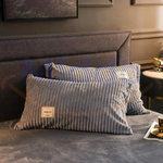 taies d'oreiller en velours polaire gris disposées sur un lit fond sombre
