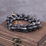Zware donkerzilveren drakenarmband op houten kist.